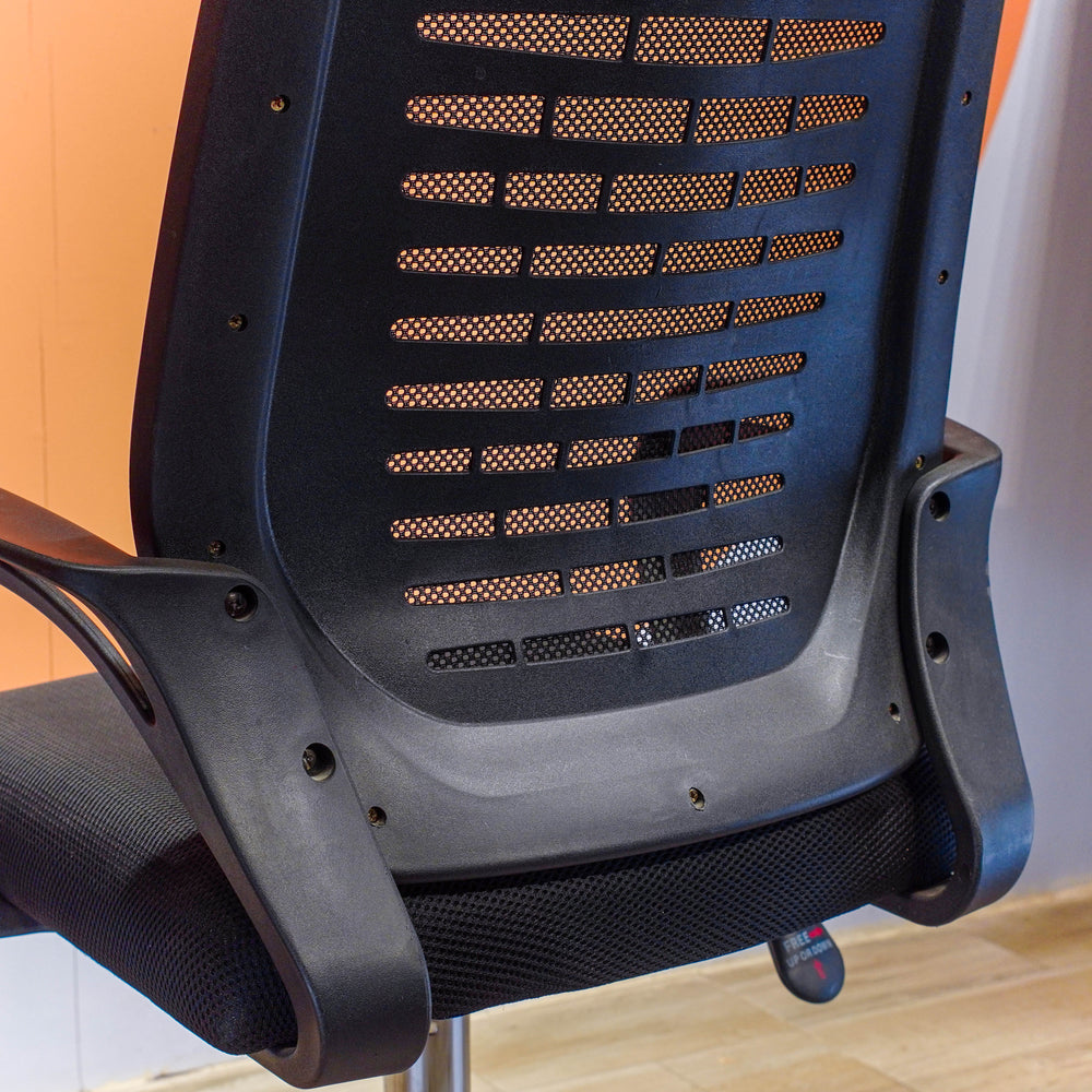 Close-up of a black office chair with mesh backrest on a wooden floor.