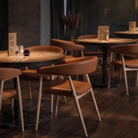 Neva Leto Chair — tan upholstered wooden armchairs arranged around tables in a restaurant.