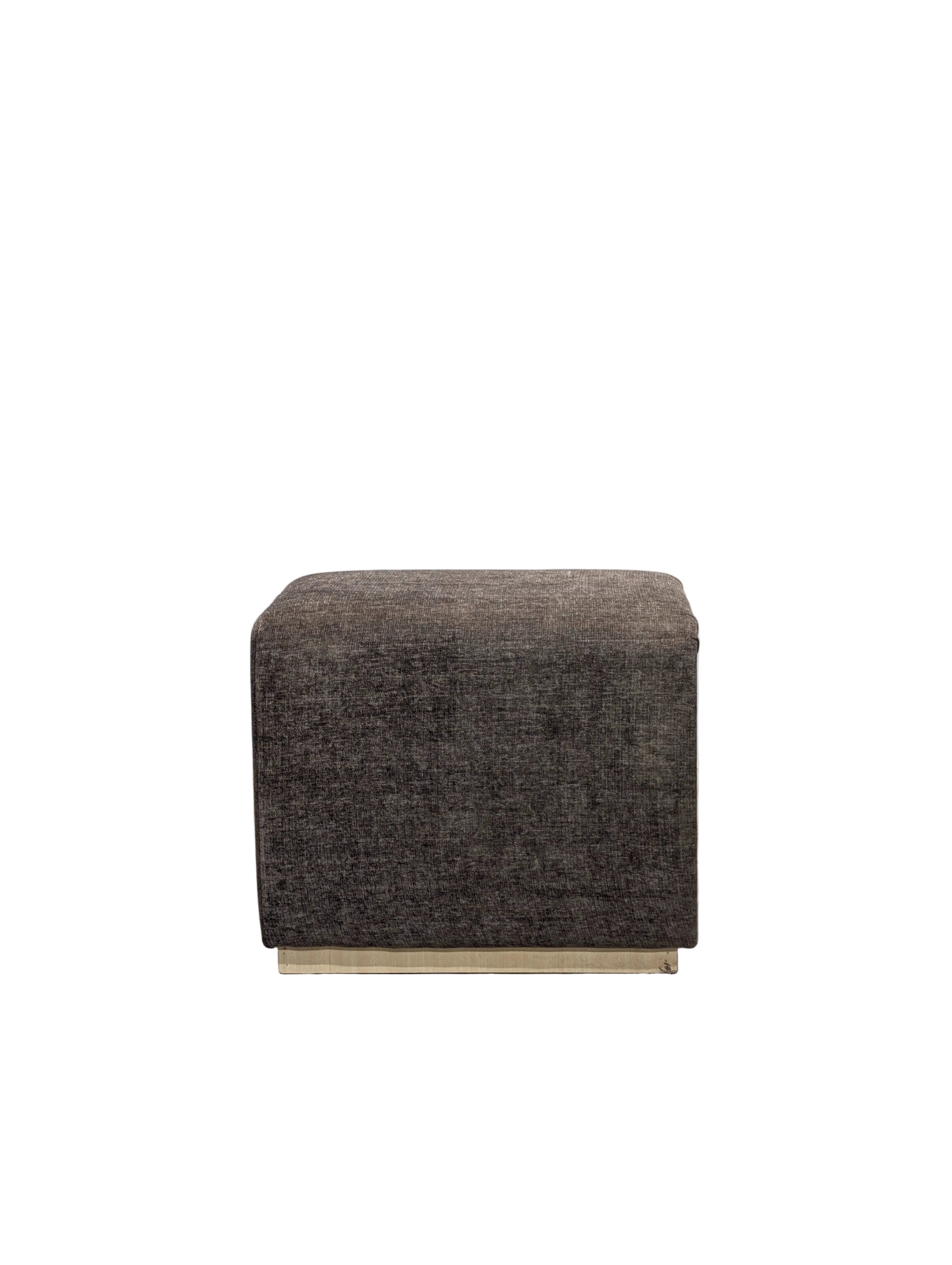 Brown cube-shaped ottoman on a wooden floor with a gray wall background